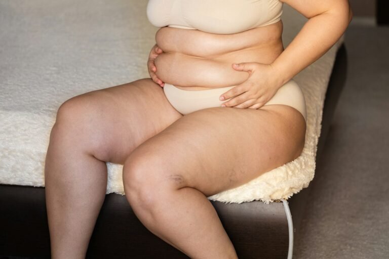 Unrecognizable fat woman sitting on edge of beige plaid in nude bra, underpants, showing squeezing